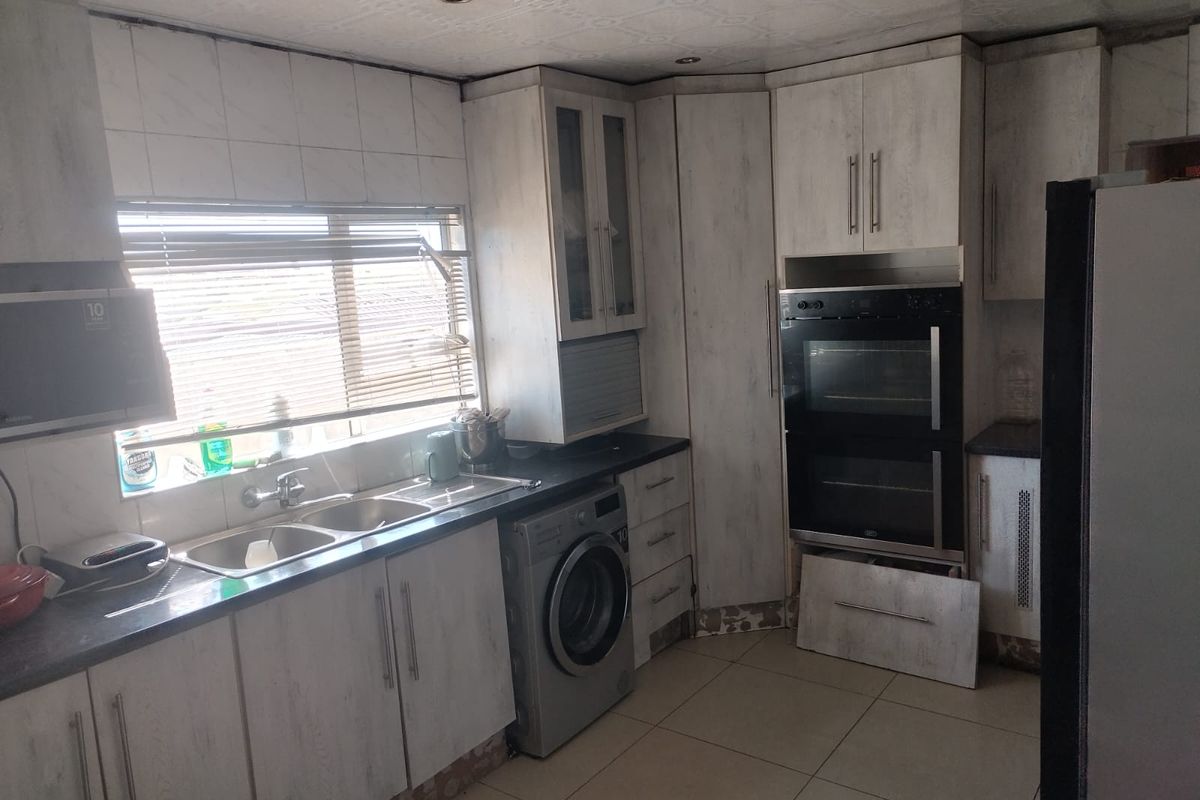 Kitchen featuring light-toned cabinetry, integrated double oven, double sink, and tiled flooring. Requires minor repairs to cabinetry and finishes.