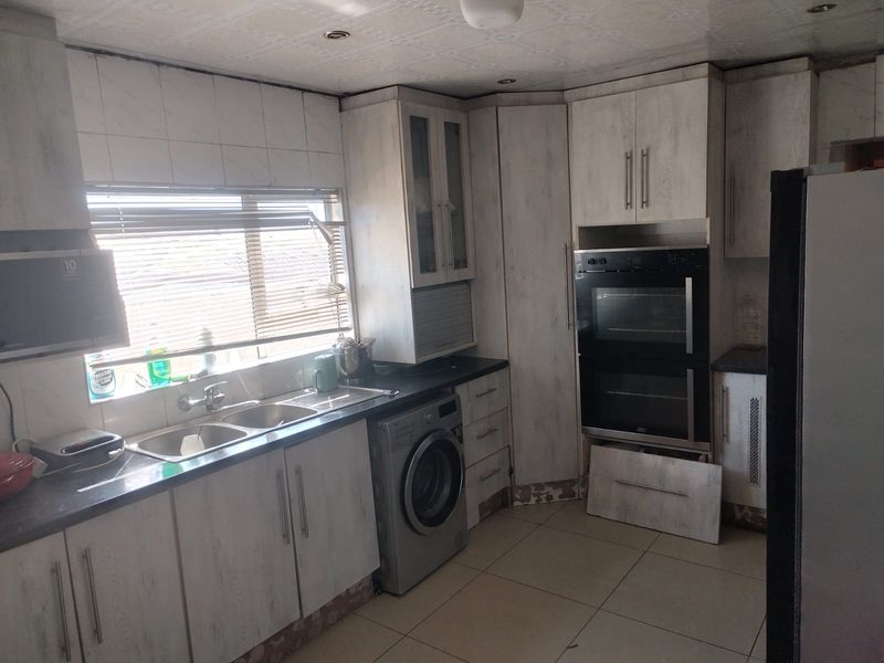Kitchen featuring light-toned cabinetry, integrated double oven, double sink, and tiled flooring. Requires minor repairs to cabinetry and finishes.