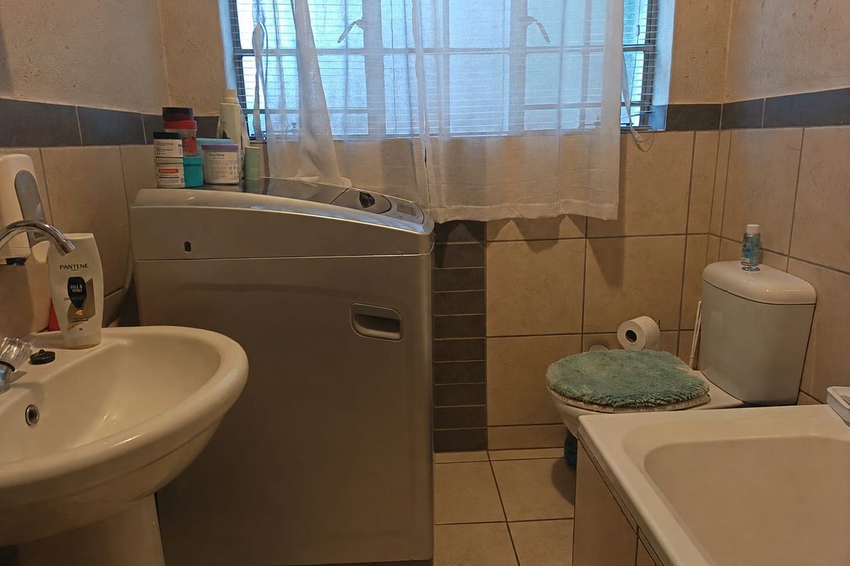 A functional bathroom featuring a pedestal basin, toilet, and bathtub with tiled finishes and a window with security bars.
