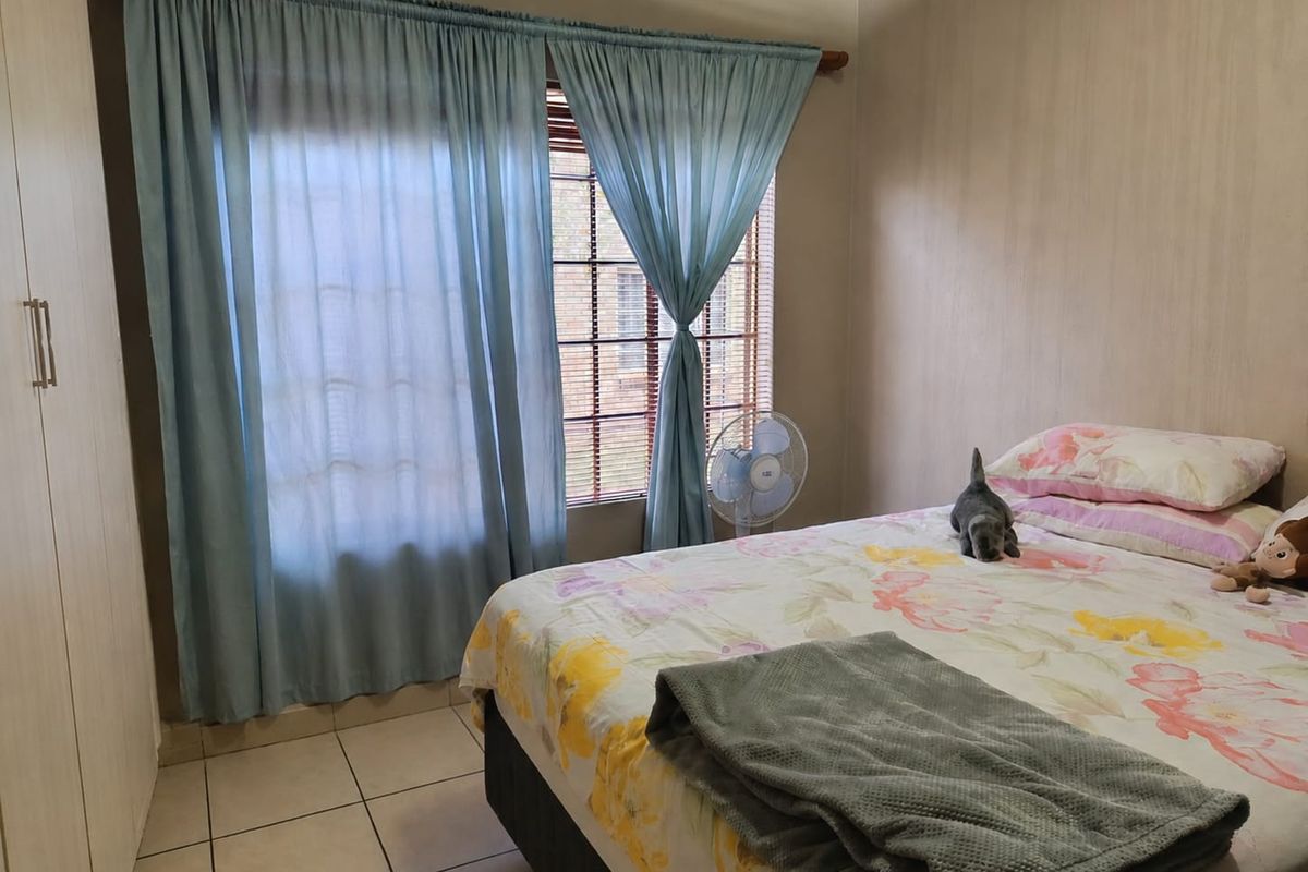 A functional bedroom featuring tiled flooring, a built-in wardrobe, and window treatments including curtains and venetian blinds.
