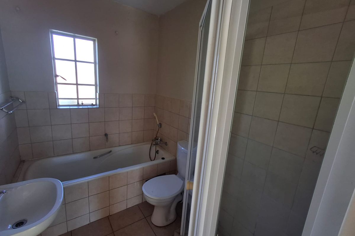 A functional bathroom featuring a bathtub, separate shower enclosure, pedestal basin, and toilet, finished with neutral wall and floor tiling.