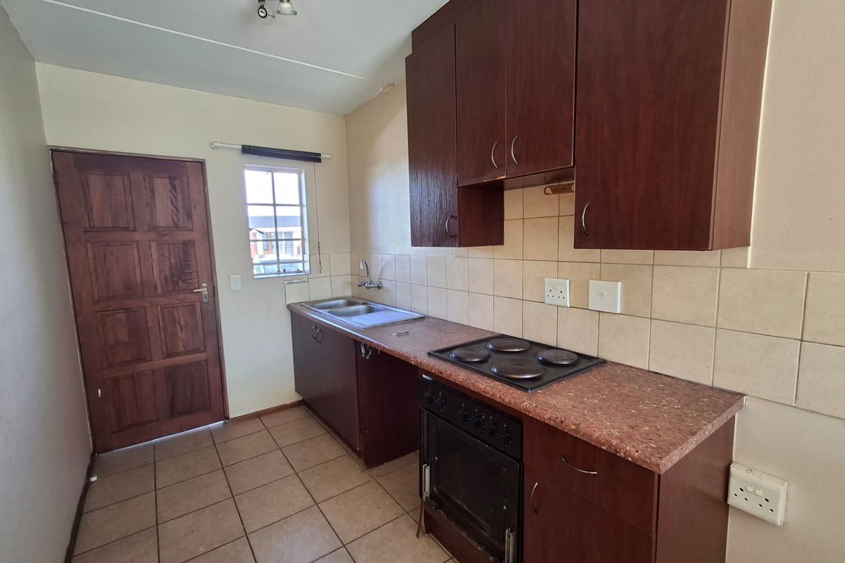 A functional kitchen featuring dark wood cabinetry, laminate countertops, a built-in oven and hob, and tiled flooring with direct exterior access.
