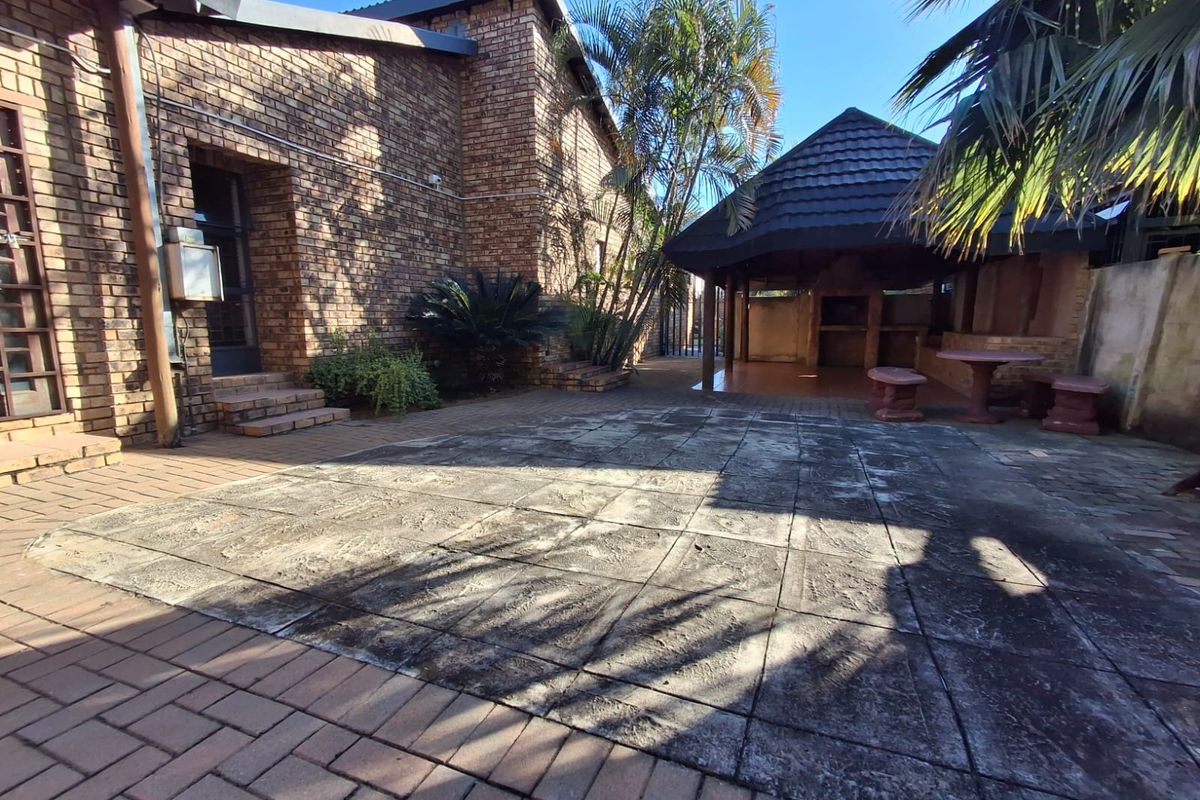 Rear exterior area featuring a paved patio, brick facade, and a thatched lapa with a built-in braai, offering potential for outdoor entertainment.
