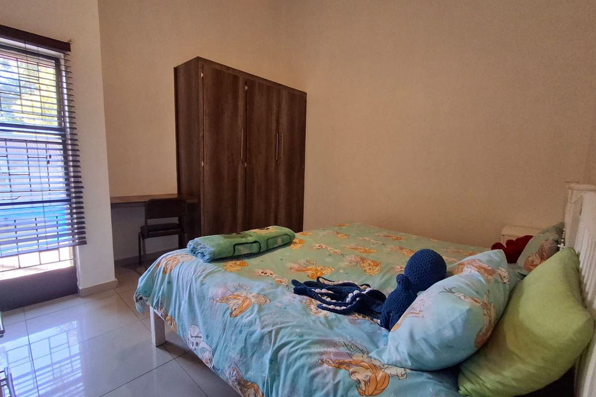 A functional bedroom featuring tiled flooring, built-in wardrobe storage, an integrated desk area, and venetian blinds for light control.