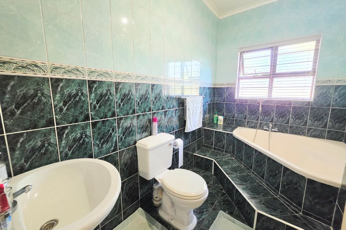 A functional bathroom featuring a built-in corner bathtub, pedestal basin, and toilet, finished with decorative green and light blue wall tiling.