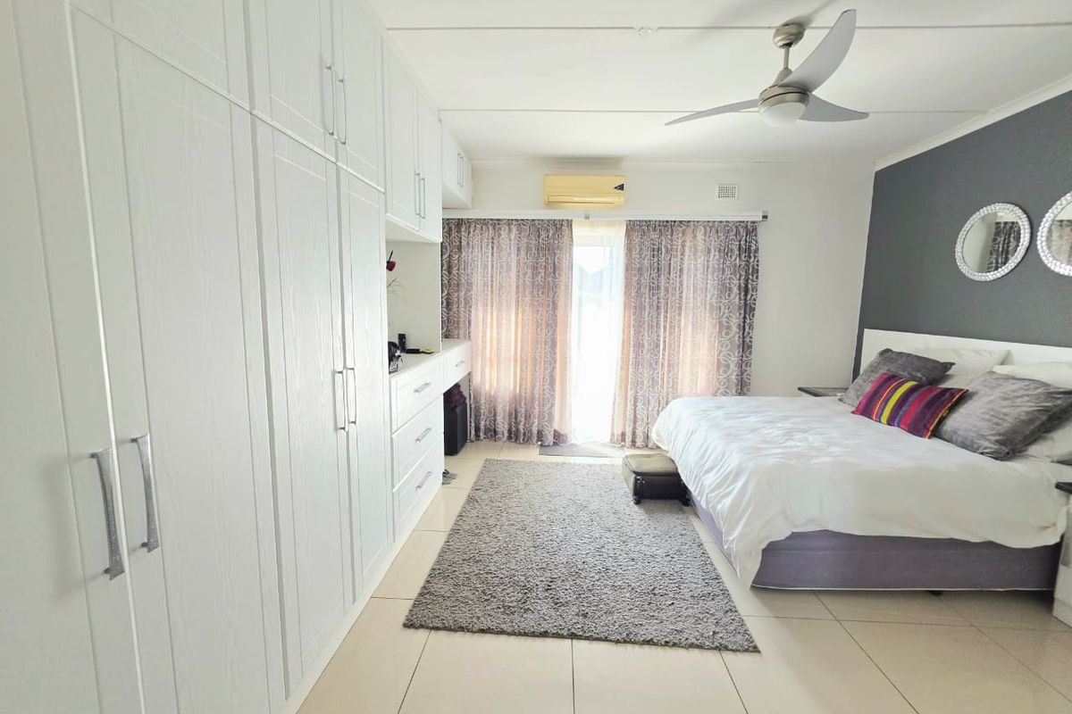 Spacious bedroom featuring extensive built-in cabinetry, tiled flooring, a ceiling fan, and a wall-mounted air conditioning unit with direct access to the outdoors.