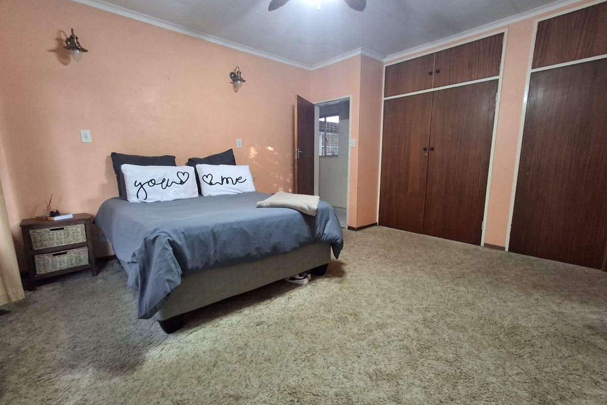 A spacious bedroom featuring built-in wooden cupboards, carpeted flooring, and a ceiling fan, offering a functional layout with potential for modern updates.