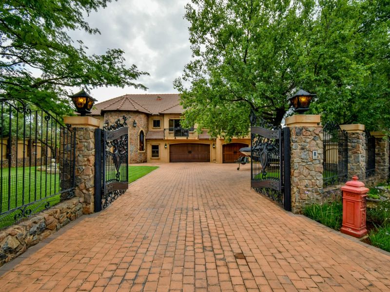 Impressive front elevation featuring a stone-clad facade, double garage, and a grand entrance with wrought iron gates and a paved driveway.