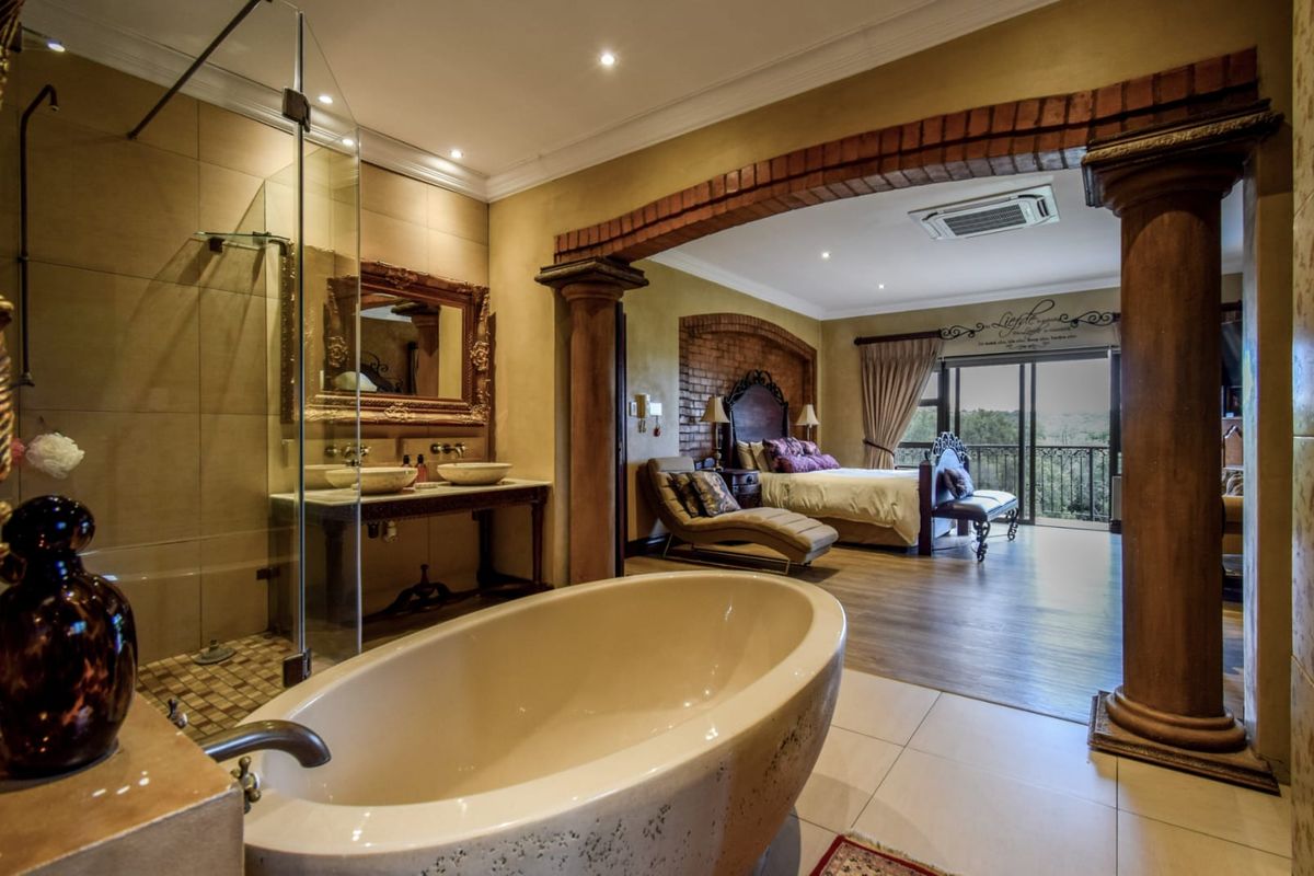Spacious open-plan bedroom suite featuring an integrated bathroom with a freestanding bathtub, glass shower, double vanity, and access to a private balcony.