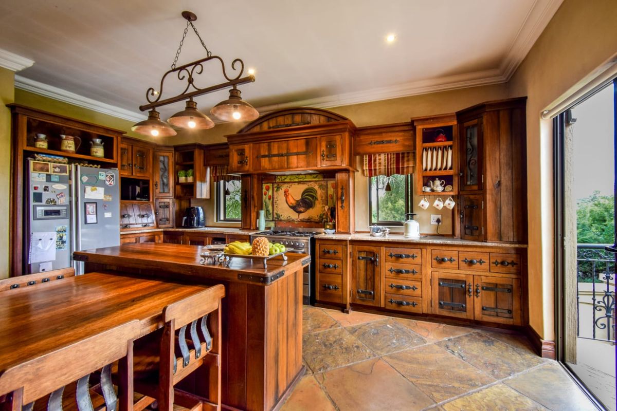 A rustic-style kitchen featuring extensive wooden cabinetry, stone flooring, a central island, and a decorative tiled backsplash with integrated cooking appliances.