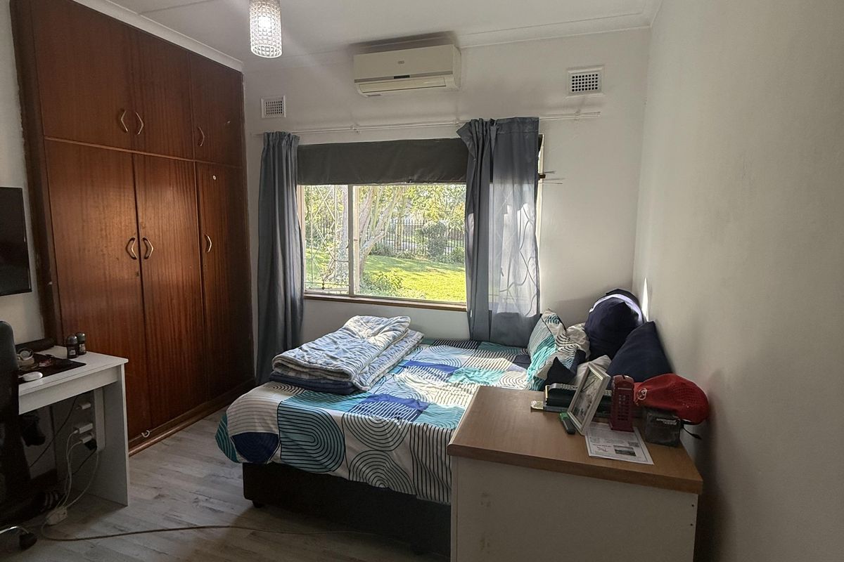 A functional bedroom featuring laminate flooring, a large built-in wooden wardrobe, and a wall-mounted air conditioning unit.