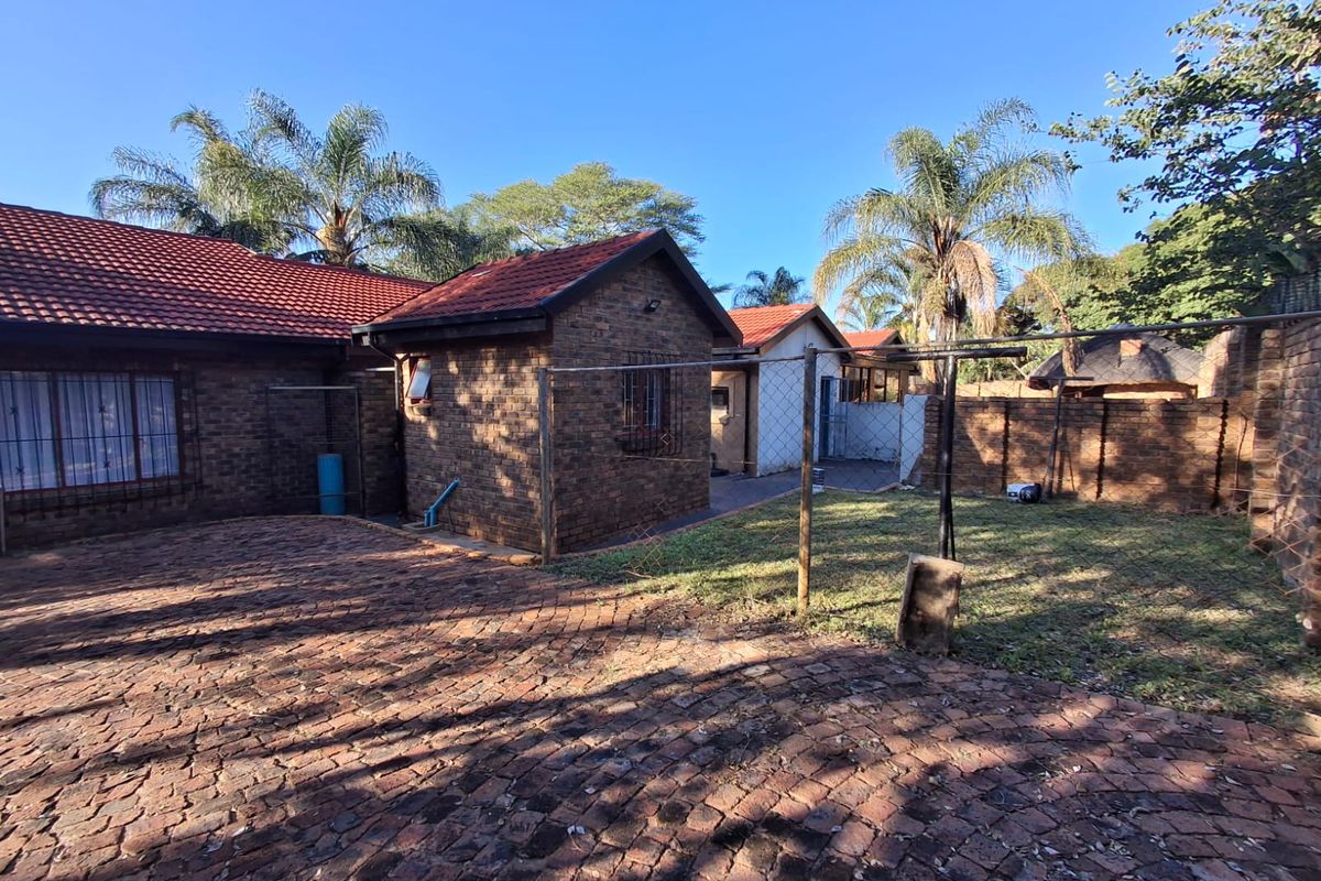 Rear view of a face-brick house featuring a tiled roof, paved driveway area, and a fenced garden space.