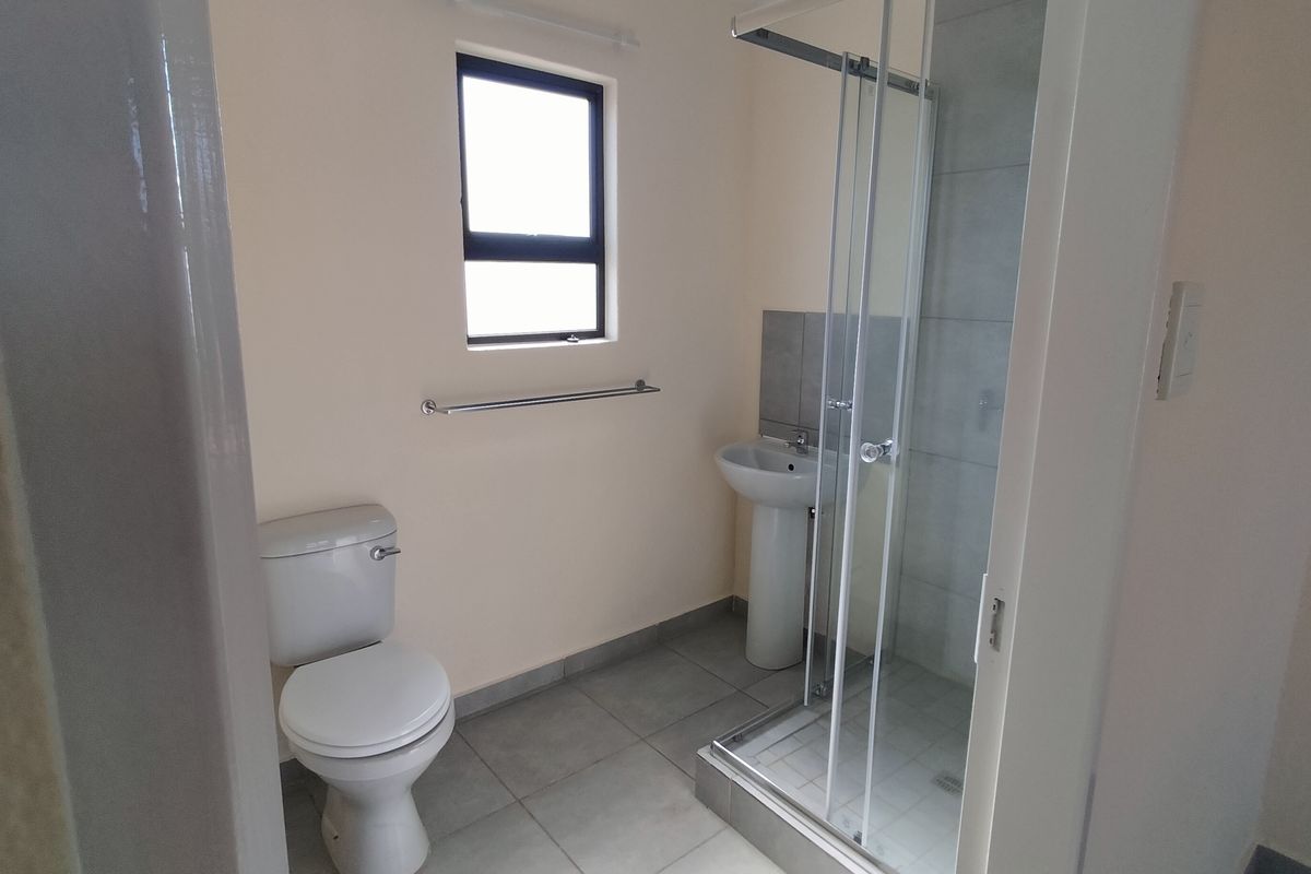 A clean, functional bathroom featuring a pedestal basin, toilet, and a glass-enclosed shower with neutral floor tiling.