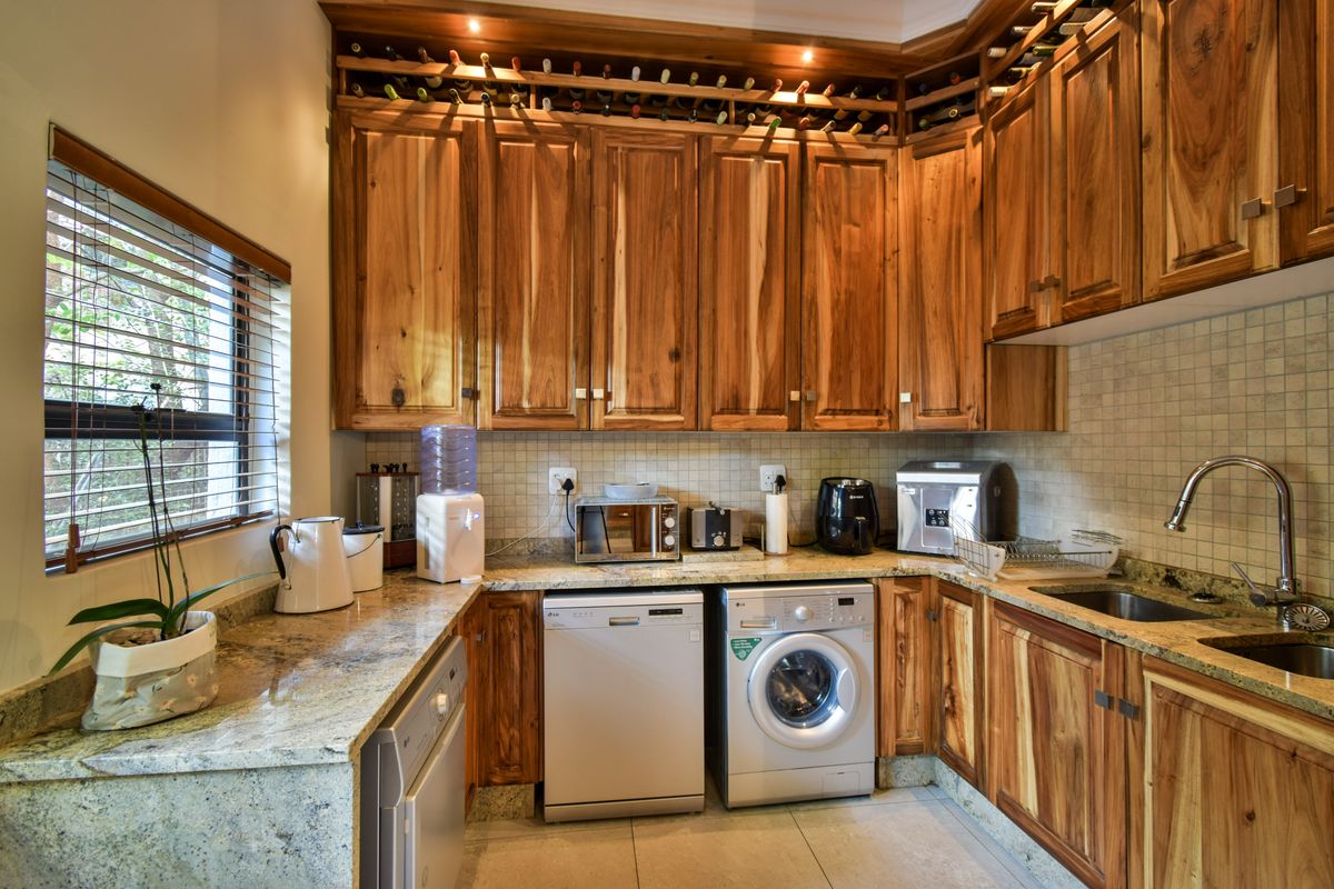 A functional kitchen featuring warm-toned wooden cabinetry, granite countertops, a tiled backsplash, and integrated laundry and dishwashing appliances.