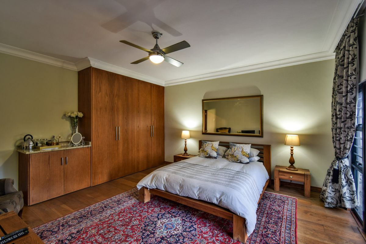 A well-maintained bedroom featuring built-in wooden cabinetry, hardwood flooring, crown molding, and a ceiling fan, creating a warm and inviting atmosphere.