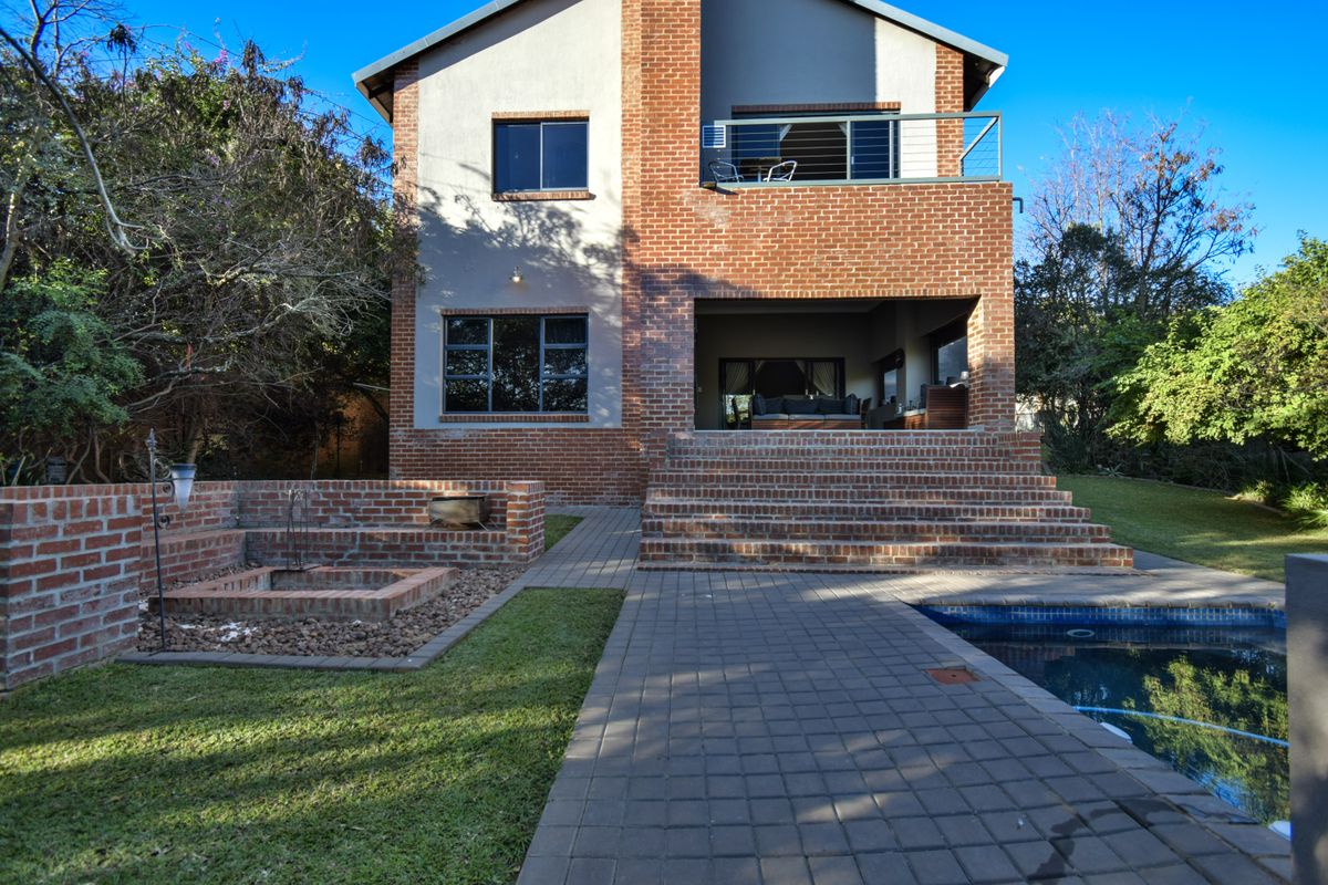 Rear view of a two-story brick house featuring a swimming pool, paved patio area, built-in fire pit, and an upper-level balcony.
