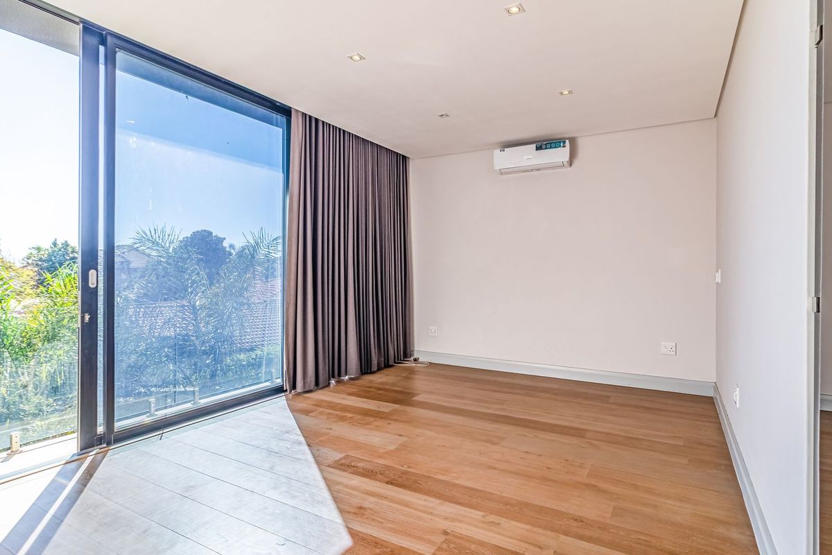 A bright, modern bedroom featuring hardwood flooring, recessed lighting, a split-system air conditioner, and large sliding glass doors opening to an outdoor view.