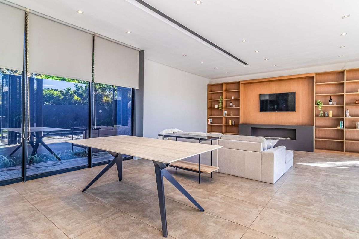 Spacious modern living room featuring large format floor tiles, built-in timber shelving, a sleek recessed fireplace, and expansive floor-to-ceiling glass doors opening to the garden.