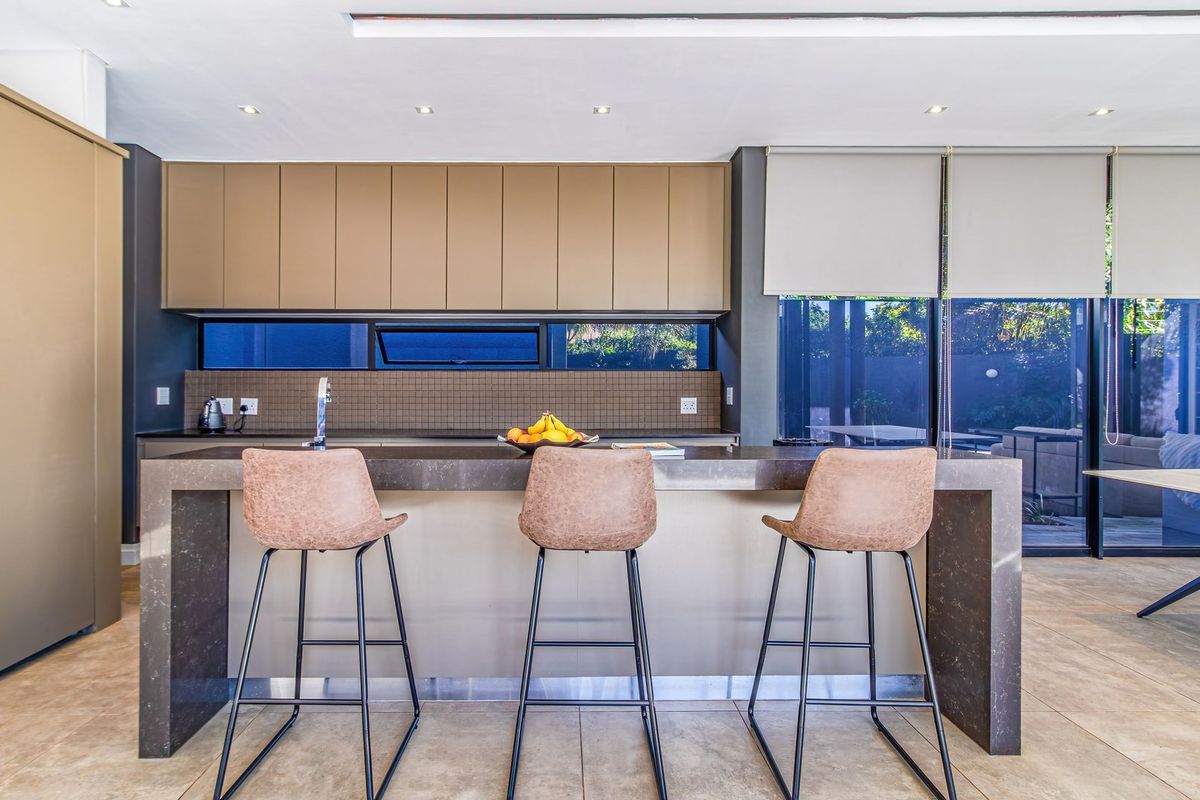 Modern kitchen featuring a large stone island, sleek built-in cabinetry, tiled splashback, and direct access to the outdoor area through sliding glass doors.