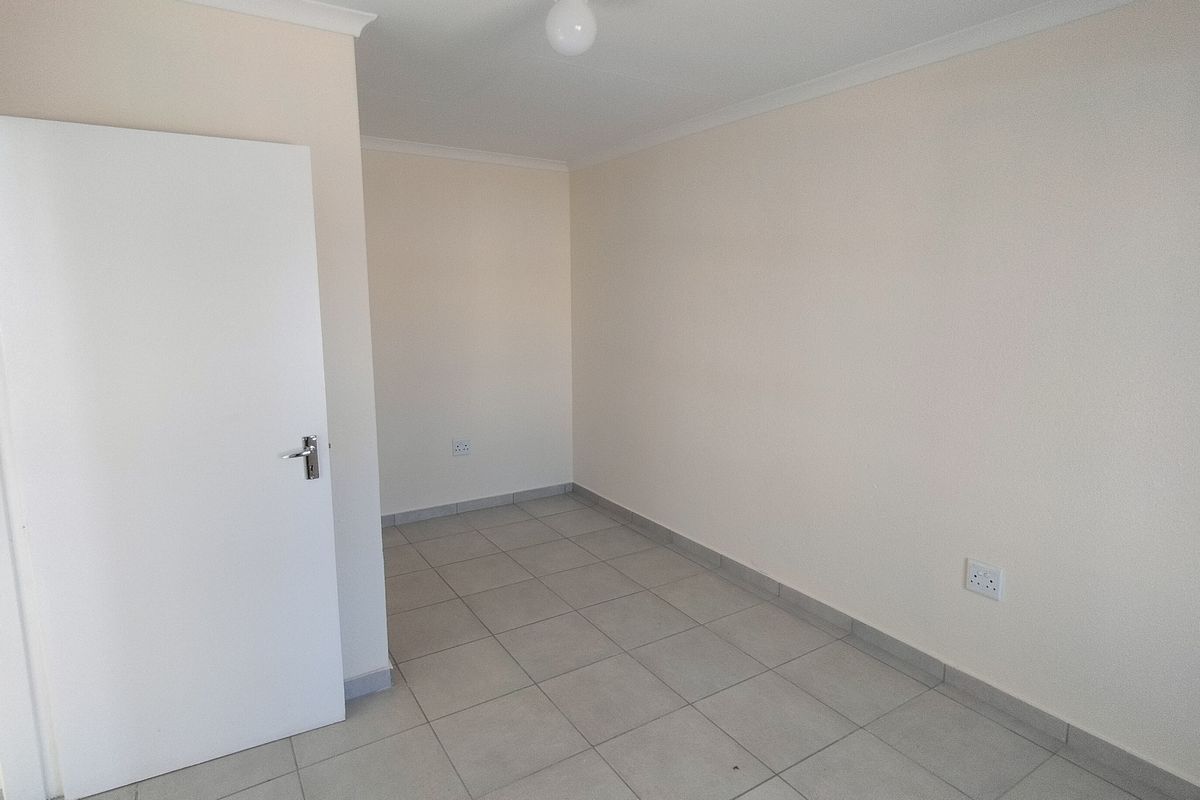 A clean, empty bedroom featuring neutral tiled flooring, white walls, and standard electrical fixtures, providing a blank canvas for personalization.
