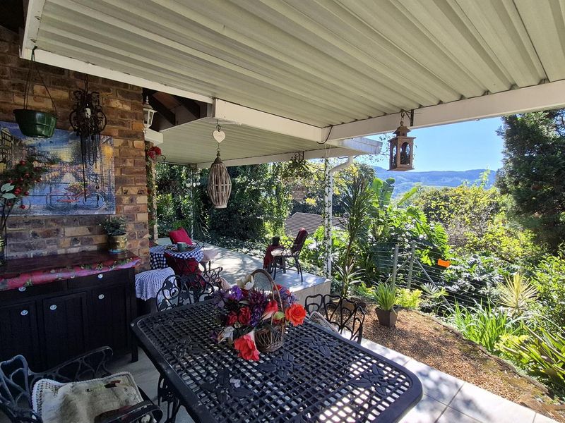 A covered outdoor patio featuring brick wall finishes and tiled flooring, offering scenic views of the surrounding garden and distant hills.