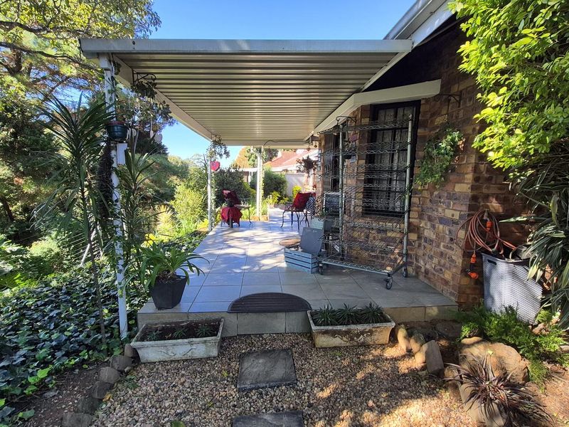 A covered outdoor patio area featuring tiled flooring, brick wall finishes, and a corrugated metal roof, overlooking a garden setting.