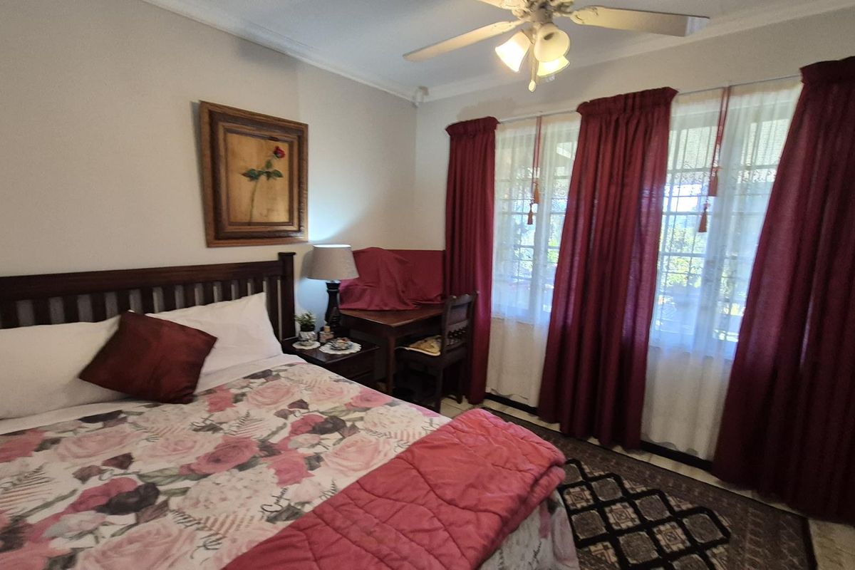 A well-lit bedroom featuring a ceiling fan, tiled flooring, and large windows with curtains, providing a comfortable and functional living space.