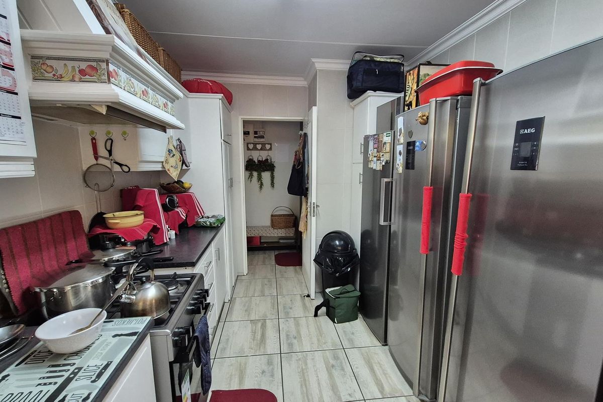 A functional kitchen featuring built-in cabinetry, tiled flooring, and a dedicated cooking area with an extractor fan, leading through to a secondary utility space.