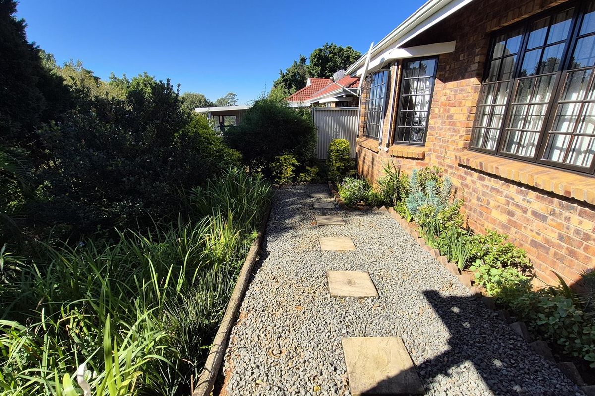 A side garden pathway featuring a gravel walkway with stone pavers, bordered by established greenery and the brick exterior of the townhouse.