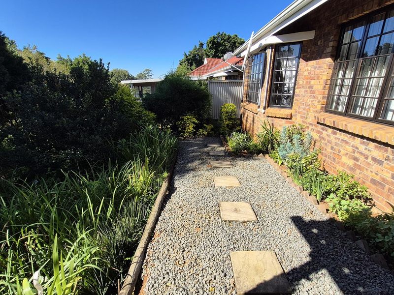 A side garden pathway featuring a gravel walkway with stone pavers, bordered by established greenery and the brick exterior of the townhouse.