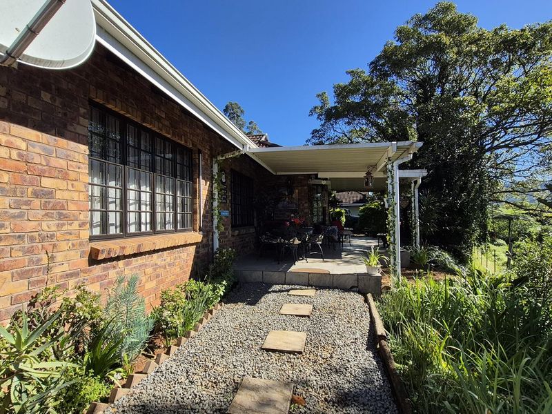 A covered patio area featuring a brick exterior, gravel pathway with stone pavers, and established garden surroundings.