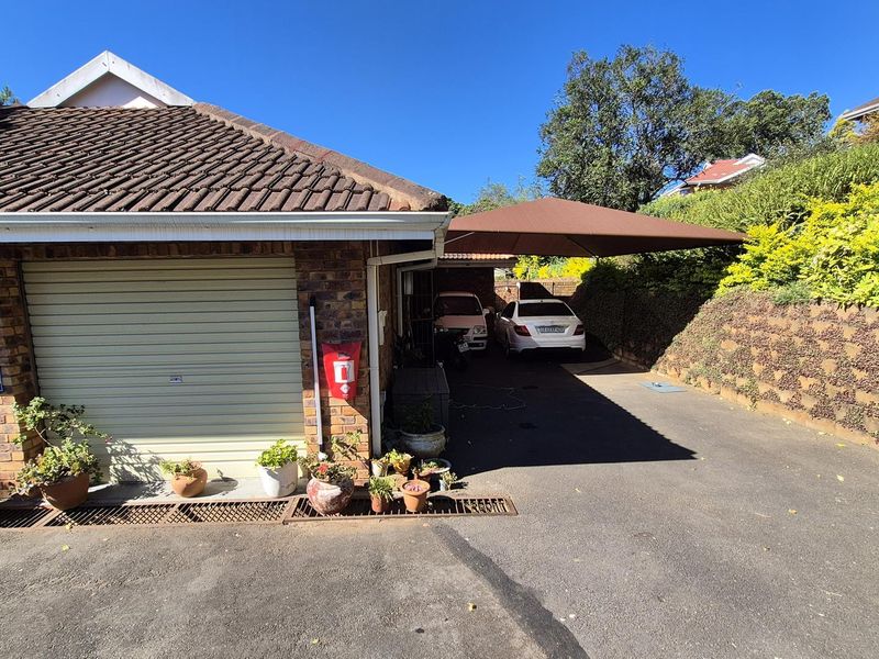 Front exterior view of the townhouse featuring a garage, paved driveway, and a shade sail covering the parking area alongside a landscaped retaining wall.
