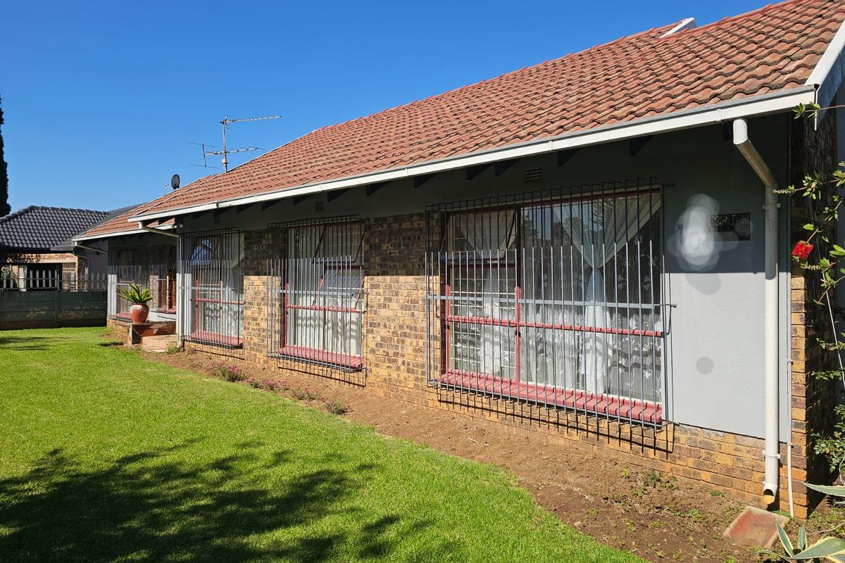 Rear view of the house featuring a terracotta tiled roof, facebrick exterior walls, and security bars on the windows, set against a lawn.