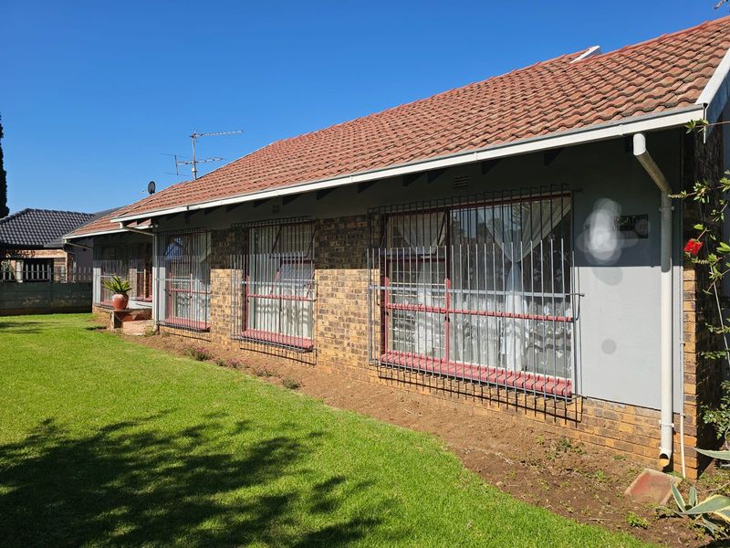 Rear view of the house featuring a terracotta tiled roof, facebrick exterior walls, and security bars on the windows, set against a lawn.