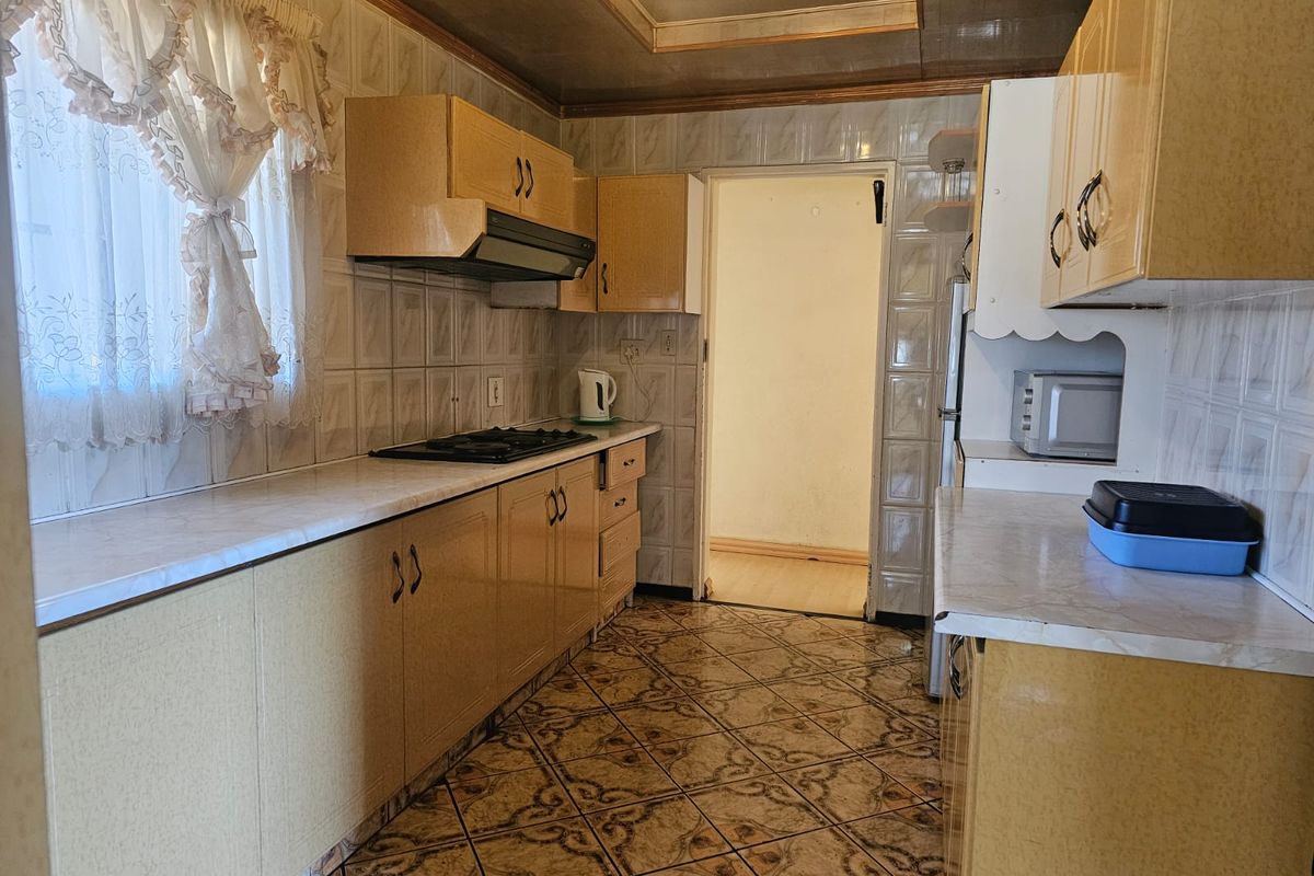 A dated kitchen featuring laminate cabinetry, gas hob with extractor fan, and ceramic tiling throughout, offering a functional layout ready for modernization.