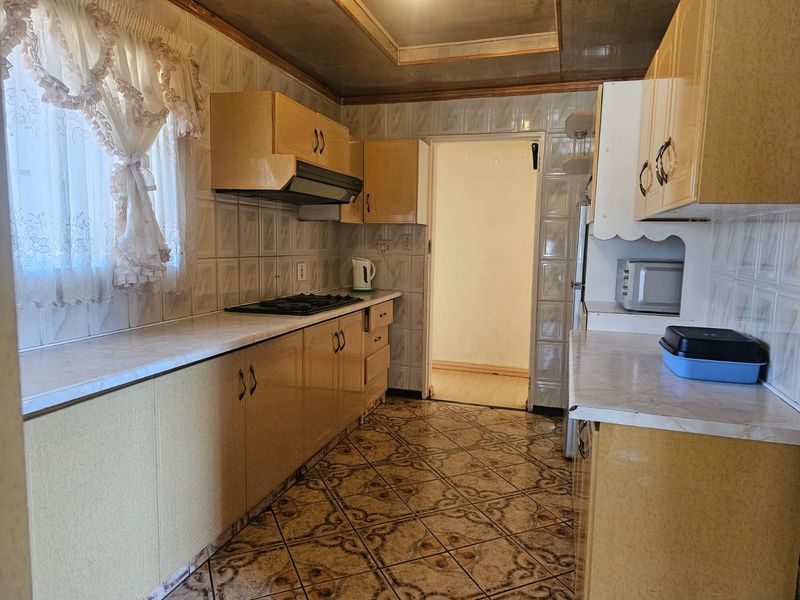 A dated kitchen featuring laminate cabinetry, gas hob with extractor fan, and ceramic tiling throughout, offering a functional layout ready for modernization.