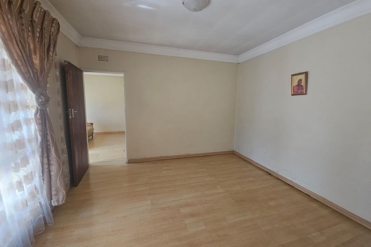 A spacious, empty bedroom featuring light-toned laminate flooring, neutral walls, and classic ceiling cornicing, offering a blank canvas for personalization.