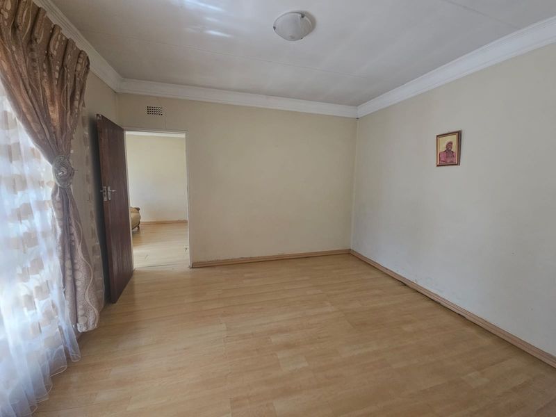 A spacious, empty bedroom featuring light-toned laminate flooring, neutral walls, and classic ceiling cornicing, offering a blank canvas for personalization.