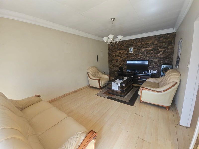 A living room featuring an exposed brick accent wall, laminate flooring, and a central pendant light fixture.