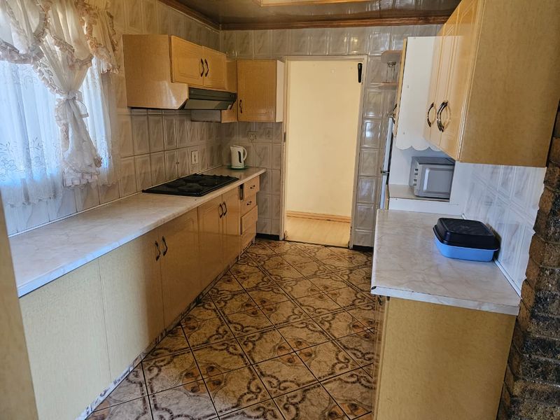 A dated kitchen featuring laminate cabinetry, built-in hob with extractor fan, and patterned floor tiles, offering significant potential for a modern renovation.