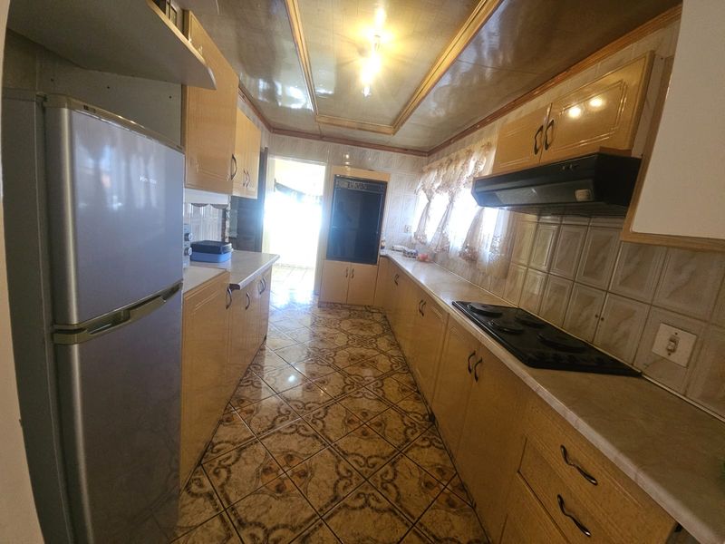 A galley-style kitchen featuring dated cabinetry, ceramic tile flooring, and built-in appliances, offering a functional layout with potential for modern renovation.