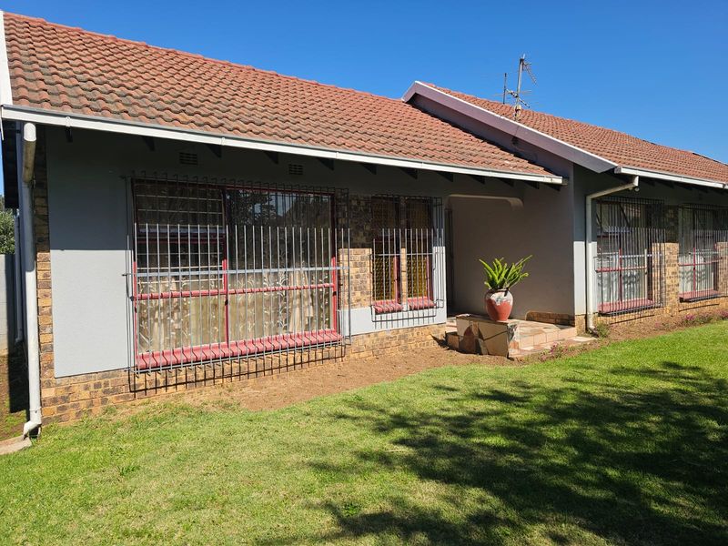 Front elevation of a single-story brick house featuring a tiled roof, security bars on windows, and a small concrete entrance area.
