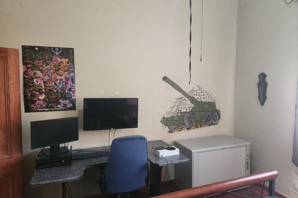 A bedroom space featuring laminate flooring and wall-mounted fixtures, currently utilized as a gaming area with visible wear on the wall surfaces.