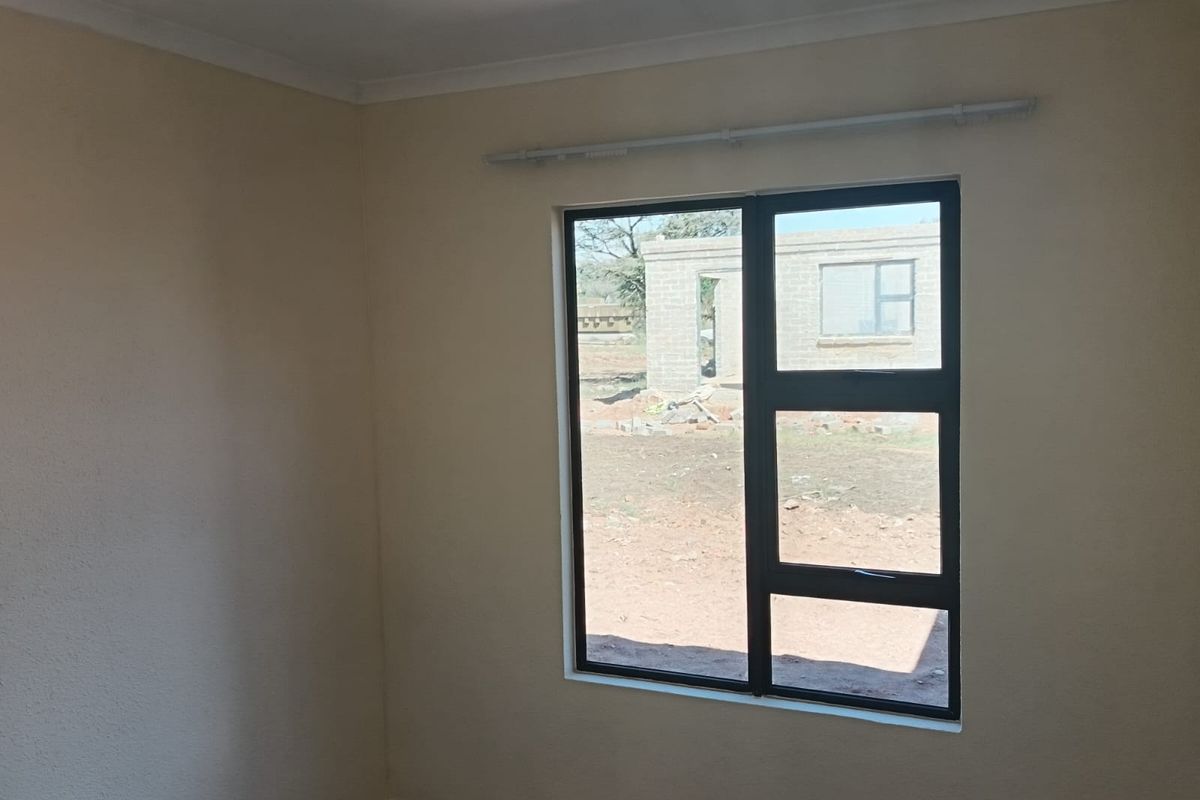 A clean, empty bedroom featuring neutral walls, tiled flooring, and a modern dark aluminium window frame with an installed curtain rail.