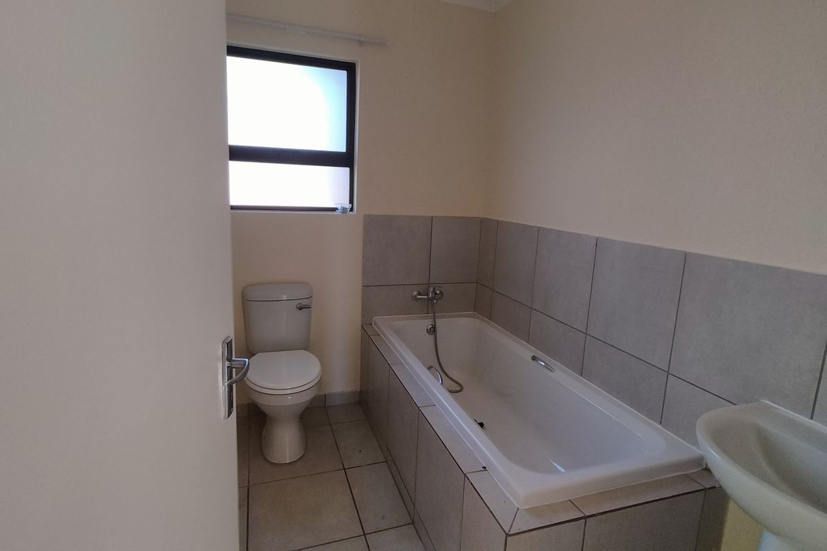 A functional bathroom featuring a built-in bathtub with tiled surround, a pedestal basin, and a standard toilet.