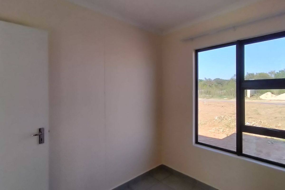 A clean, empty bedroom featuring neutral walls, tiled flooring, and a large aluminium-framed window with views of the surrounding area.