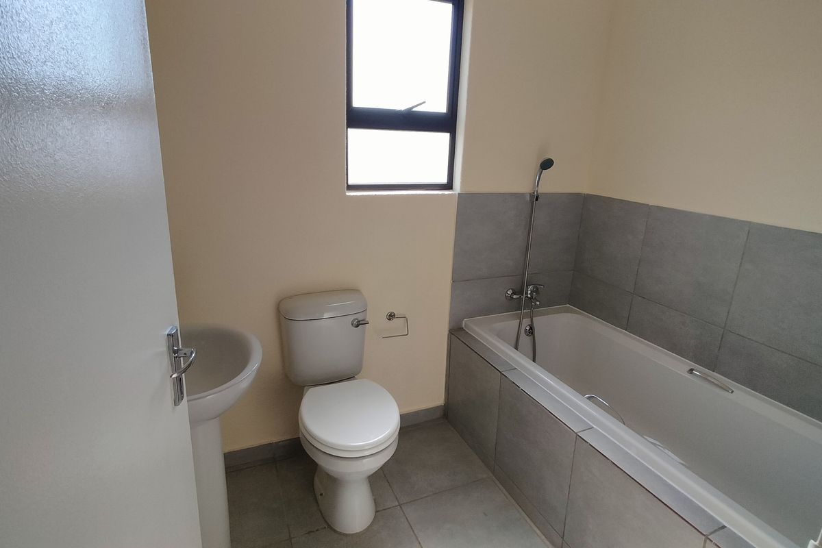 A clean, functional bathroom featuring a pedestal basin, toilet, and a bathtub with a shower mixer, finished with neutral wall paint and grey floor tiles.