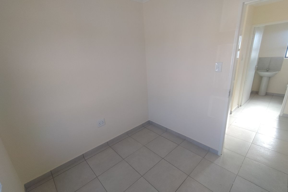 A clean, empty bedroom featuring neutral tiled flooring and coving, with a view into an adjacent bathroom area.