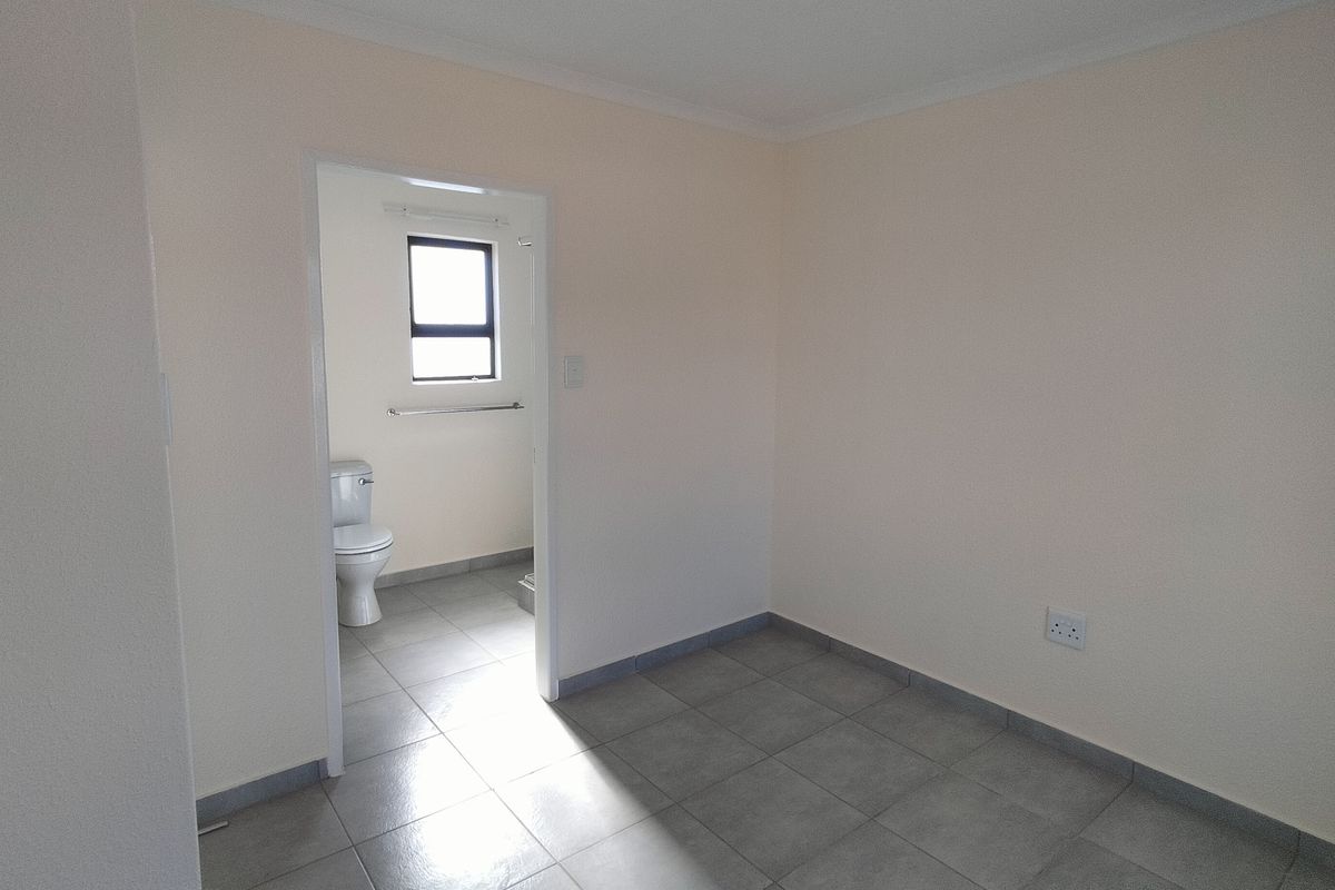 A clean, empty bedroom featuring neutral walls, tiled flooring, and an adjoining en-suite bathroom with a toilet.