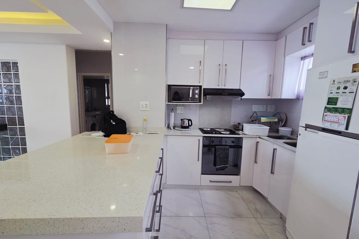 Modern kitchen featuring white cabinetry, stone countertops, integrated appliances, and a breakfast bar, complemented by stylish glass block wall detailing.